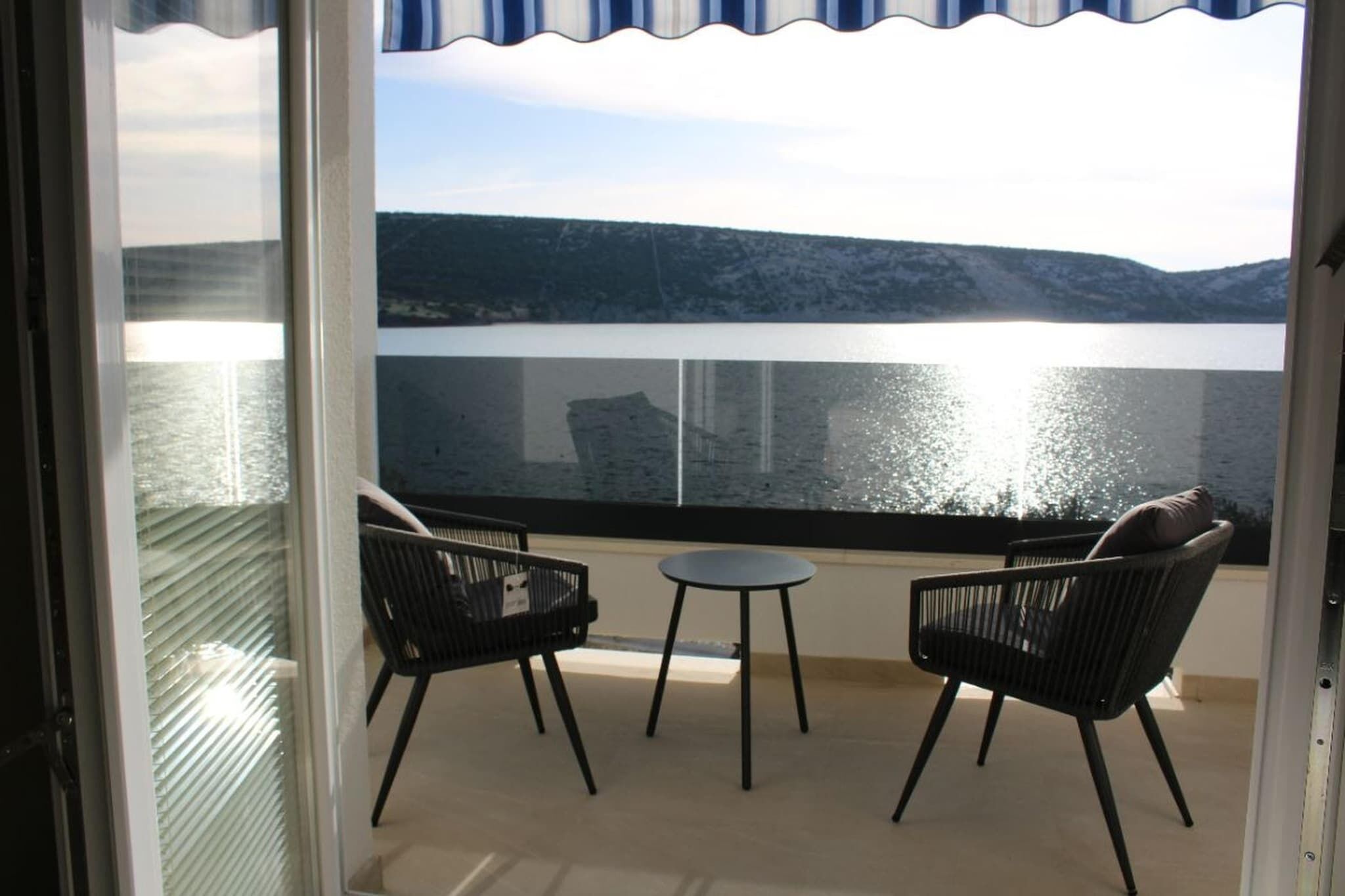 Un balcon avec deux chaises et une petite table, donnant sur une étendue d’eau et des collines.