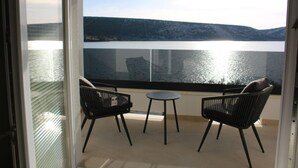 Een balkon met twee stoelen en een klein tafeltje, met uitzicht op een waterpartij en heuvels.