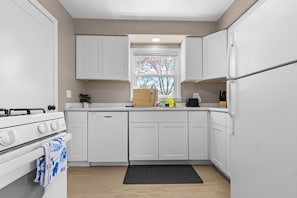 A modern kitchen with white cabinets, a stove, a dishwasher, and a window with a view of trees. - Spacious Home with Game Room, Backyard and Parking (Rockford)