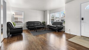Ein Wohnzimmer mit Holzboden, zwei schwarzen Ledersofas, einem Couchtisch und einer Topfpflanze.