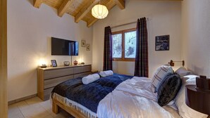 A bedroom with a wooden bed, a TV on the wall, a bedside table, and a window with curtains. - Chalet Renard Roux - La Tzoumaz, 4 Vallees (La Tzoumaz)