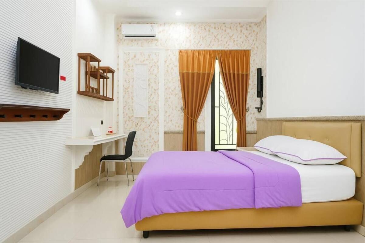 Una habitación de hotel con una cama, un escritorio, una silla, un televisor y una ventana con cortinas.