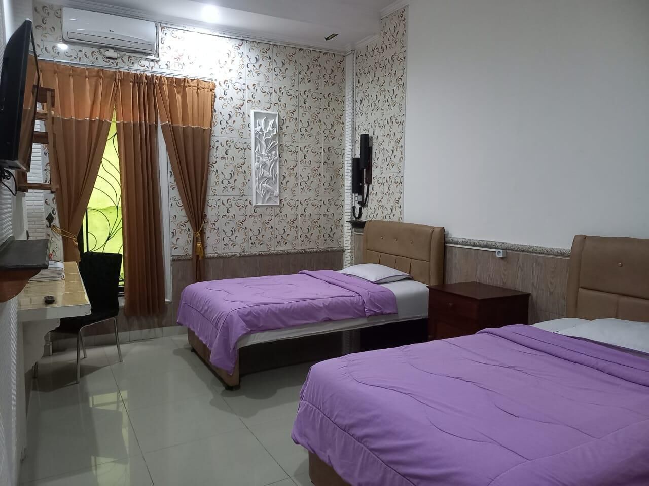 A hotel room with two beds, a desk, a chair, and a TV.