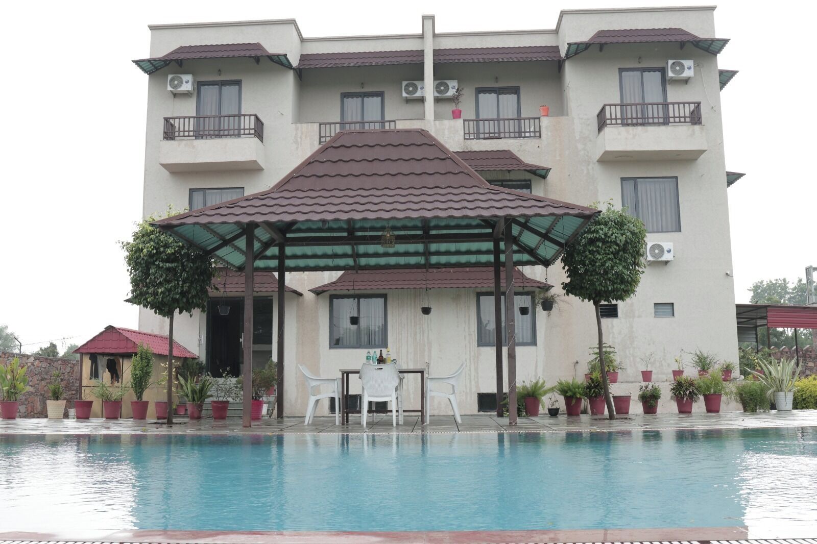 A multi-story building with a swimming pool, a covered outdoor seating area, and potted plants.