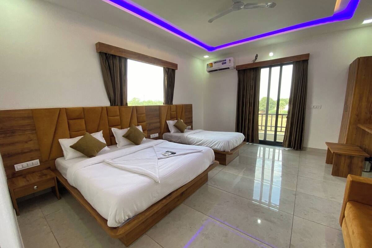Habitación de hotel con dos camas, ventilador de techo, unidad de aire acondicionado y balcón con cortinas.
