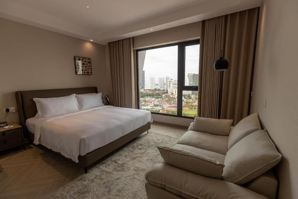 A hotel room with a large bed, a sofa, a view of a cityscape, and a window with curtains.
