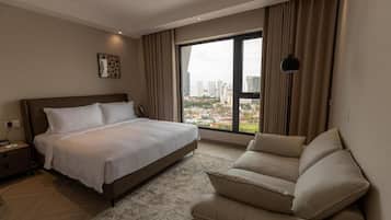 A hotel room with a large bed, a sofa, a view of a cityscape, and a window with curtains.