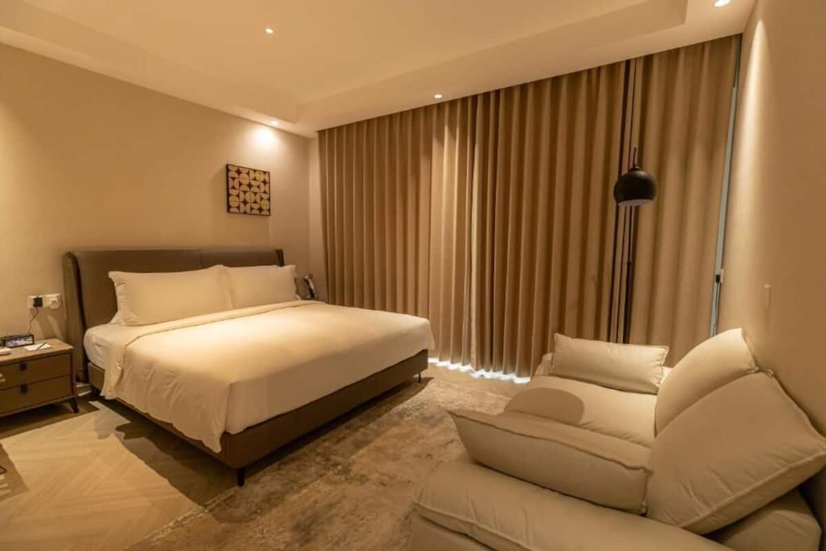 A modern hotel room with a large bed, a sofa, a bedside table, and a floor lamp.