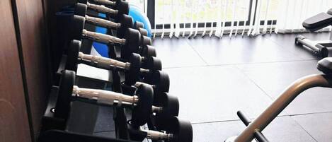 A gym with a row of dumbbells, a blue exercise ball, and a water bottle.