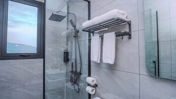 Un baño moderno con cabina de ducha de vidrio, un perchero con toallas, un inodoro y un espejo grande.
