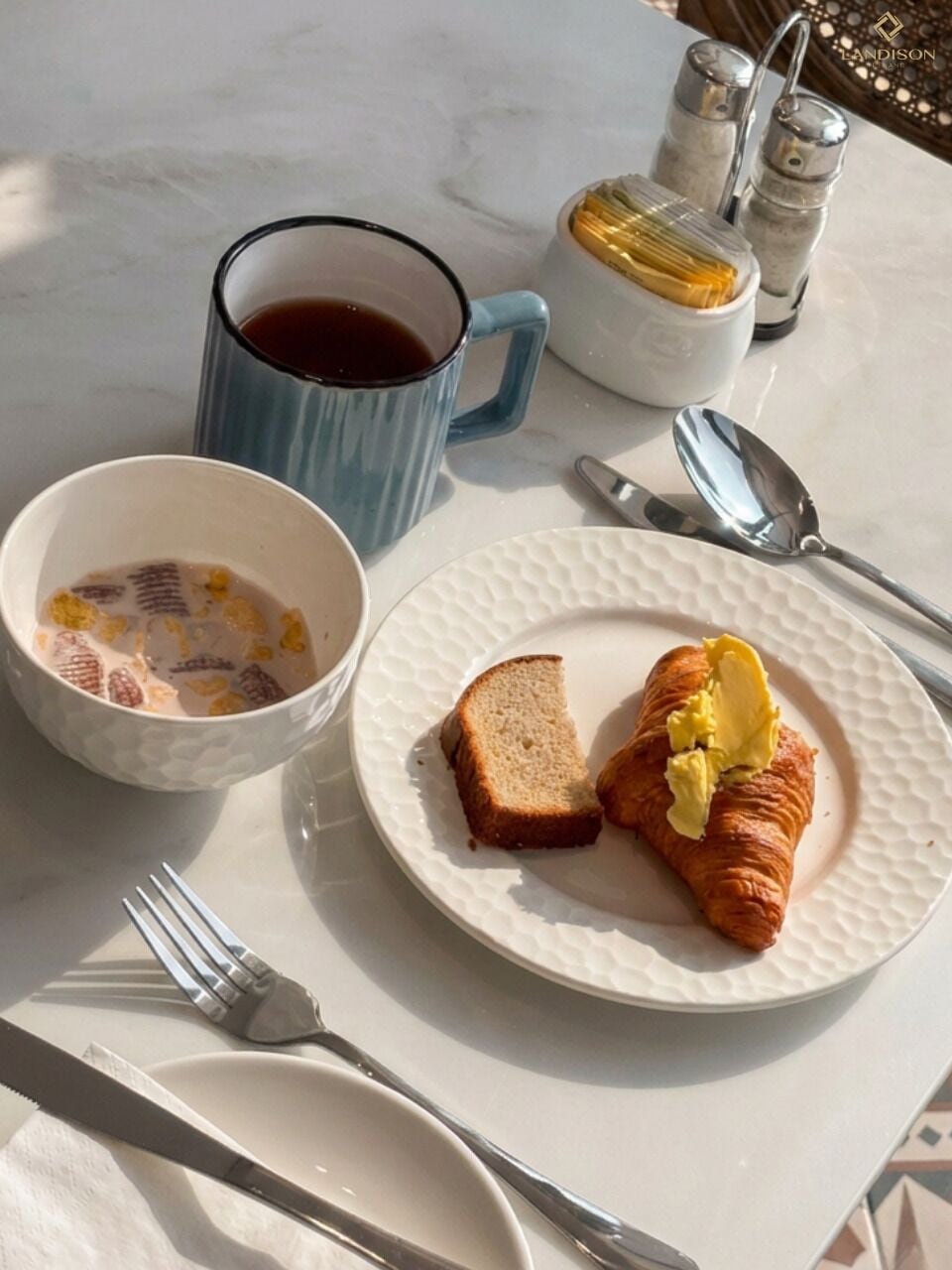 Una colazione con un piatto di croissant e pane tostato, una tazza di caffè e una ciotola di cereali.