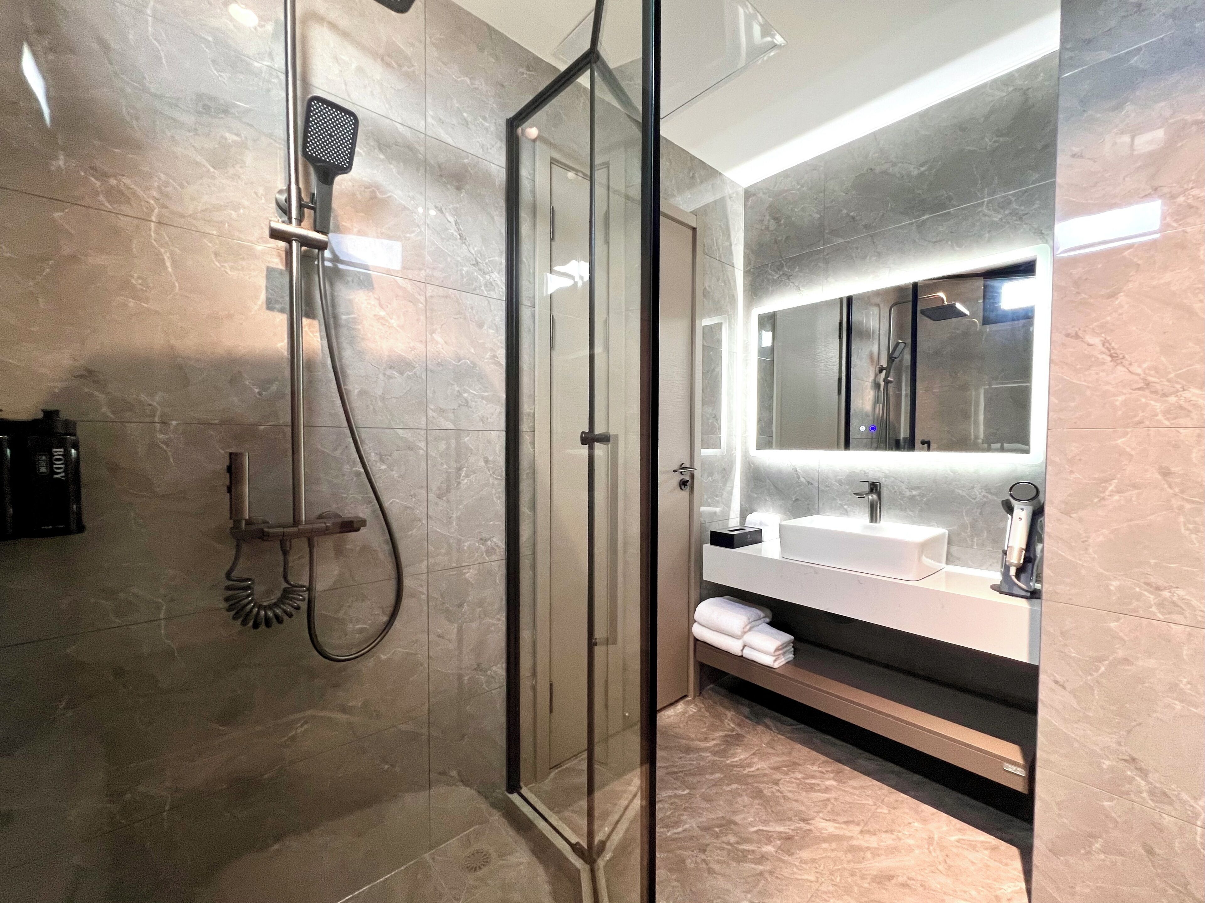 A modern bathroom with a glass shower enclosure, a large mirror, and a vanity with a sink and towel storage.