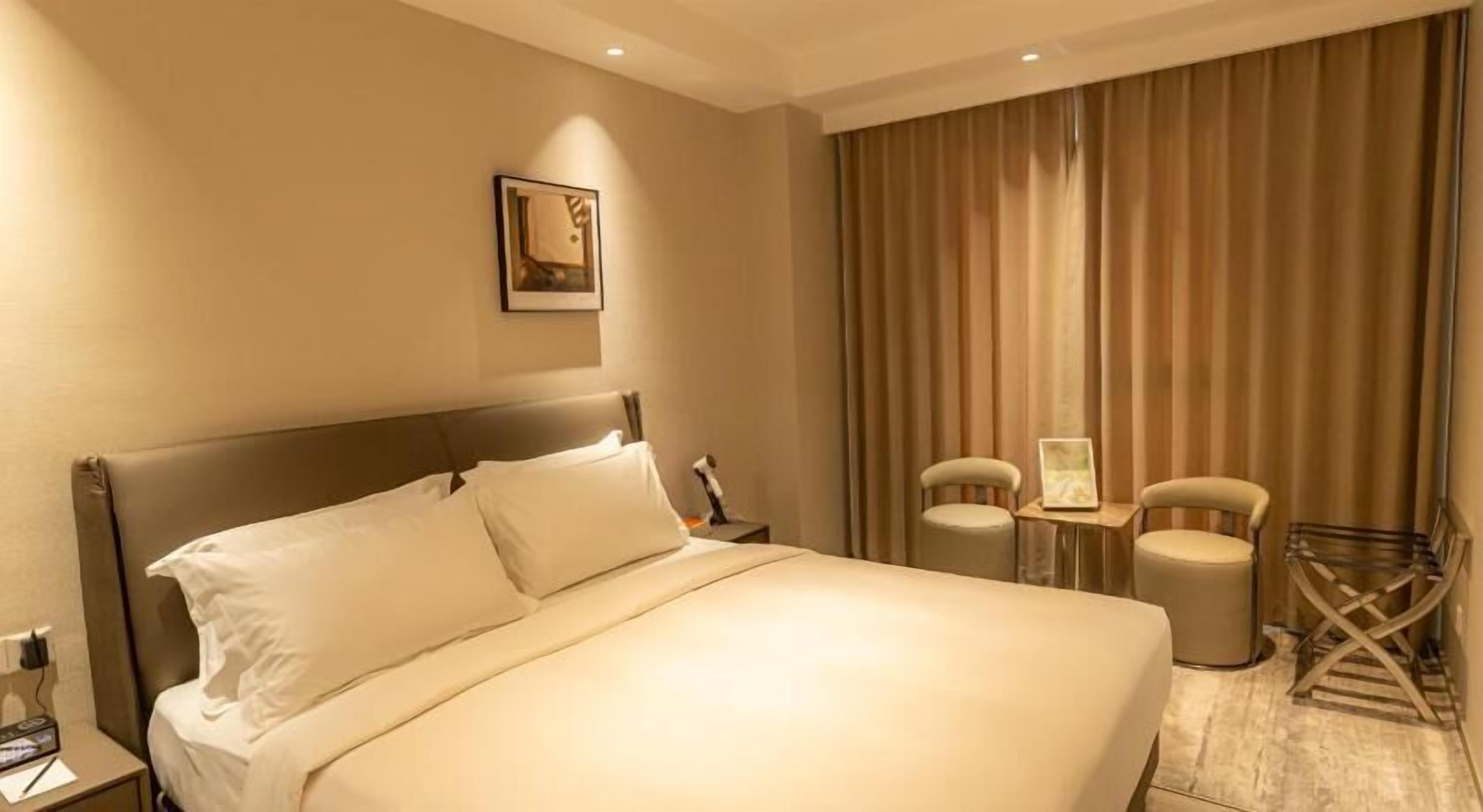 Ein Hotelzimmer mit einem großen Bett, zwei Stühlen, einem kleinen Tisch und einem Vorhang.