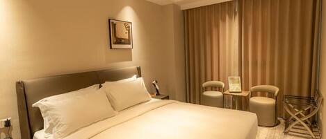 Ein Hotelzimmer mit einem großen Bett, zwei Stühlen, einem kleinen Tisch und einem Vorhang.
