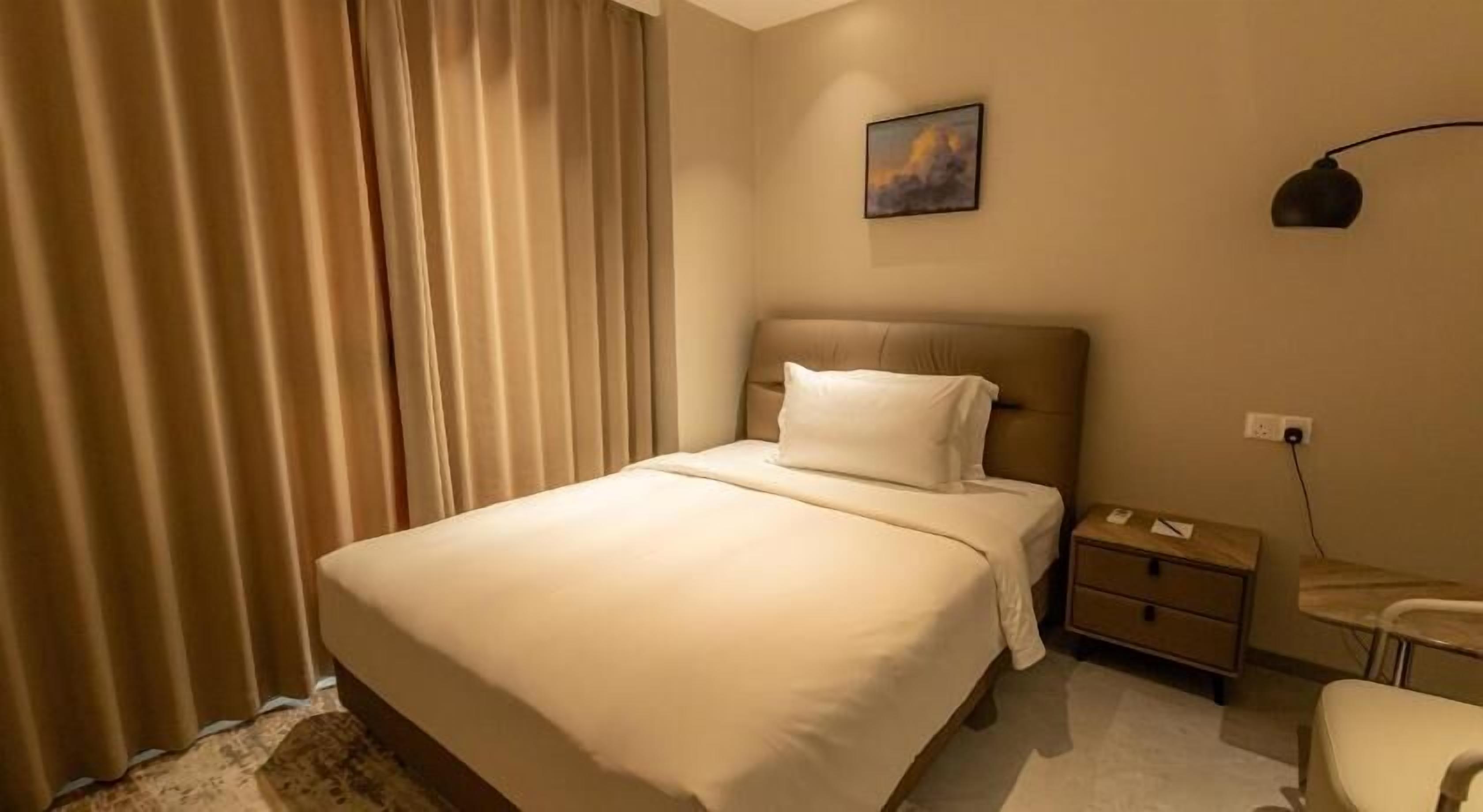 A hotel room with a bed, a nightstand, a lamp, and a painting on the wall.