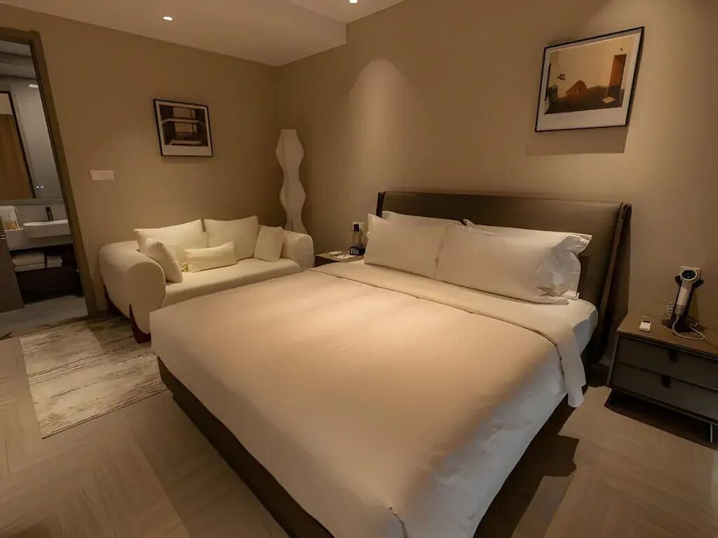A modern hotel room with a large bed, a sofa, a nightstand, and a mirror.