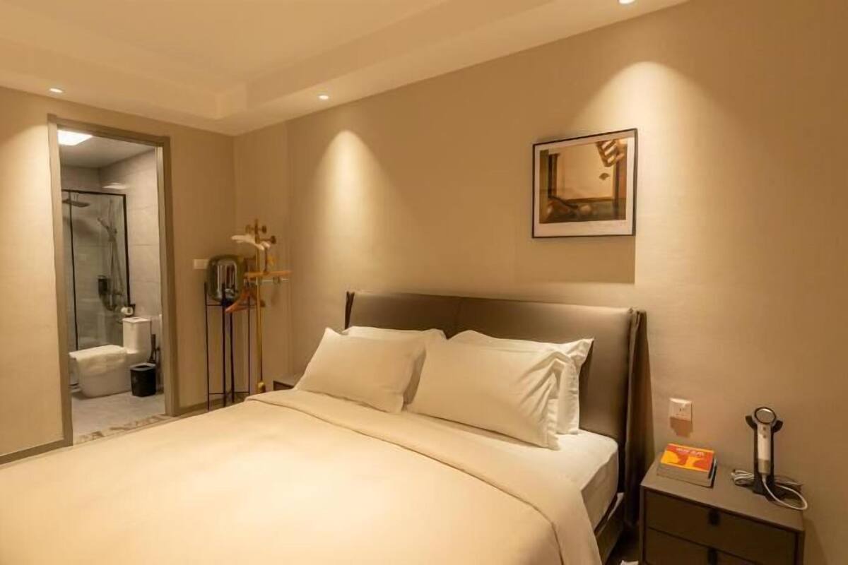 A hotel room with a bed, bedside table, and a framed picture on the wall.