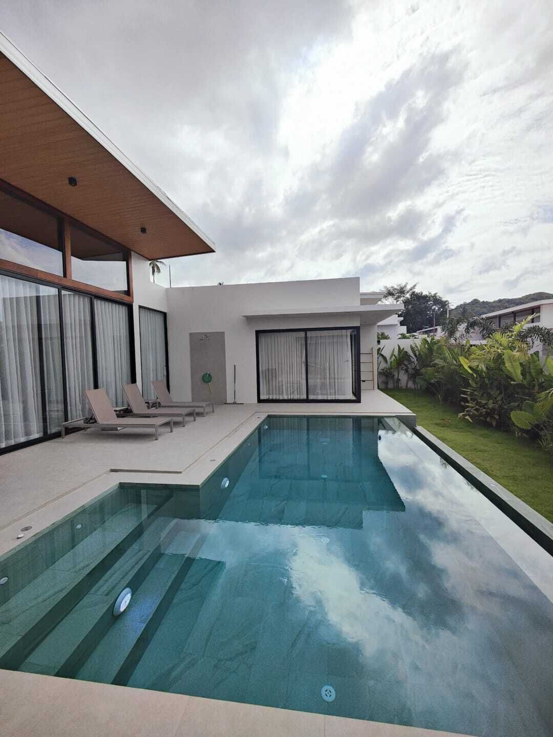 Una casa moderna con piscina, un porche cubierto y un jardín bien cuidado.