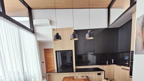 A modern kitchen with a wooden dining table and chairs, a black countertop, and pendant lights. - Samui Luxury villas-BySamui Rental  (Bueang Sam Phan)