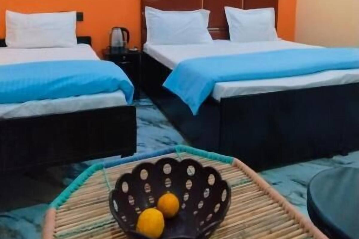 A hotel room with two beds, a small table with a bowl of fruit, and orange walls.