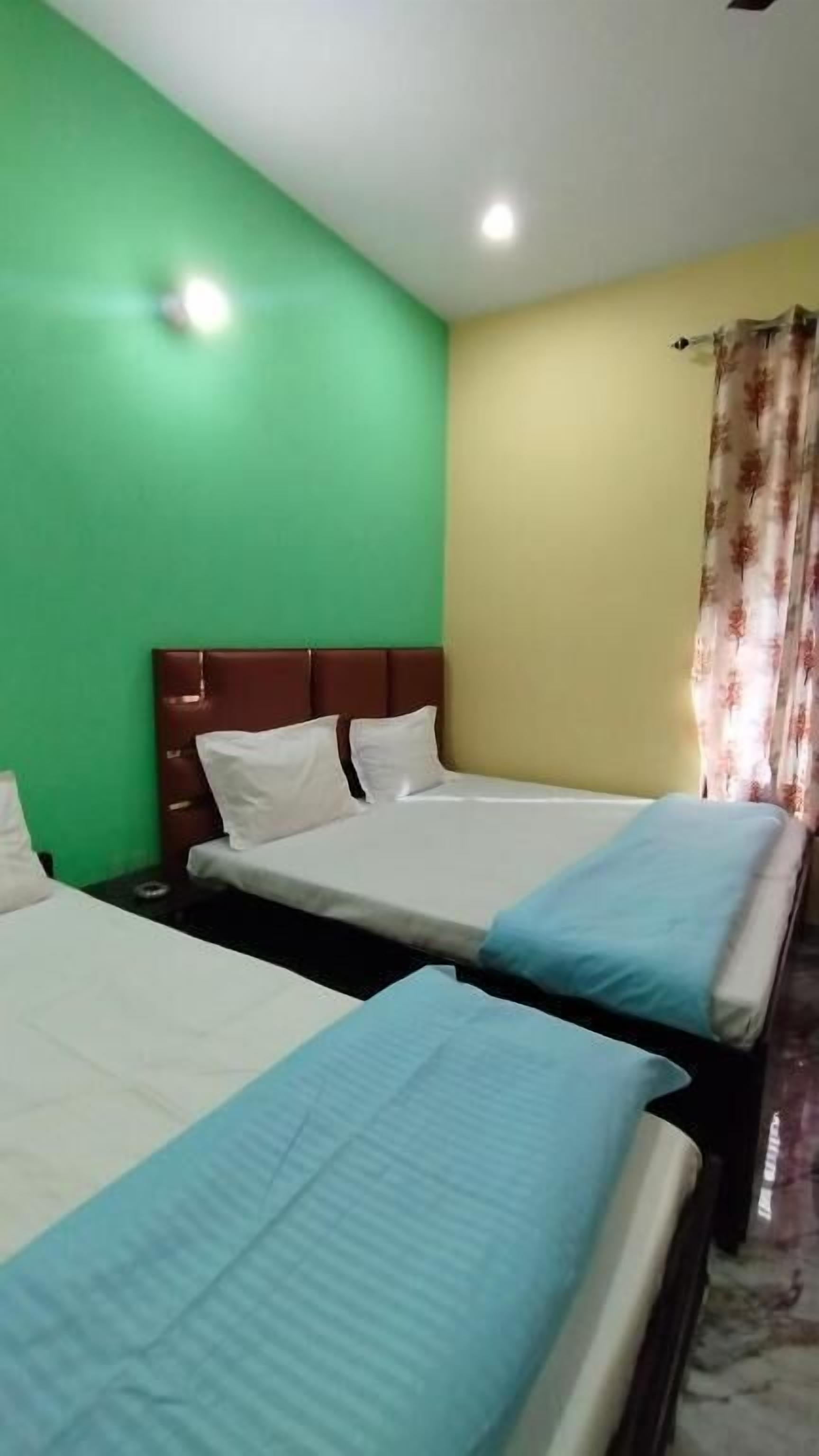 A hotel room with two beds, green and yellow walls, and a floral curtain.