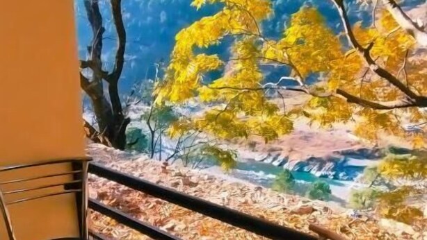 A balcony with a view of autumn leaves and a table with a bowl of fruit. - Yamunotri Darshan Resort By Preet rS (Rajgarhi)