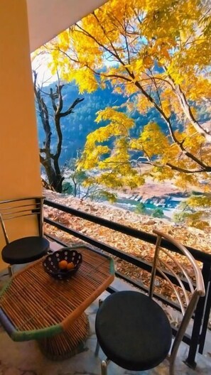 A balcony with a view of autumn leaves and a table with a bowl of fruit. - Yamunotri Darshan Resort By Preet rS (Rajgarhi)
