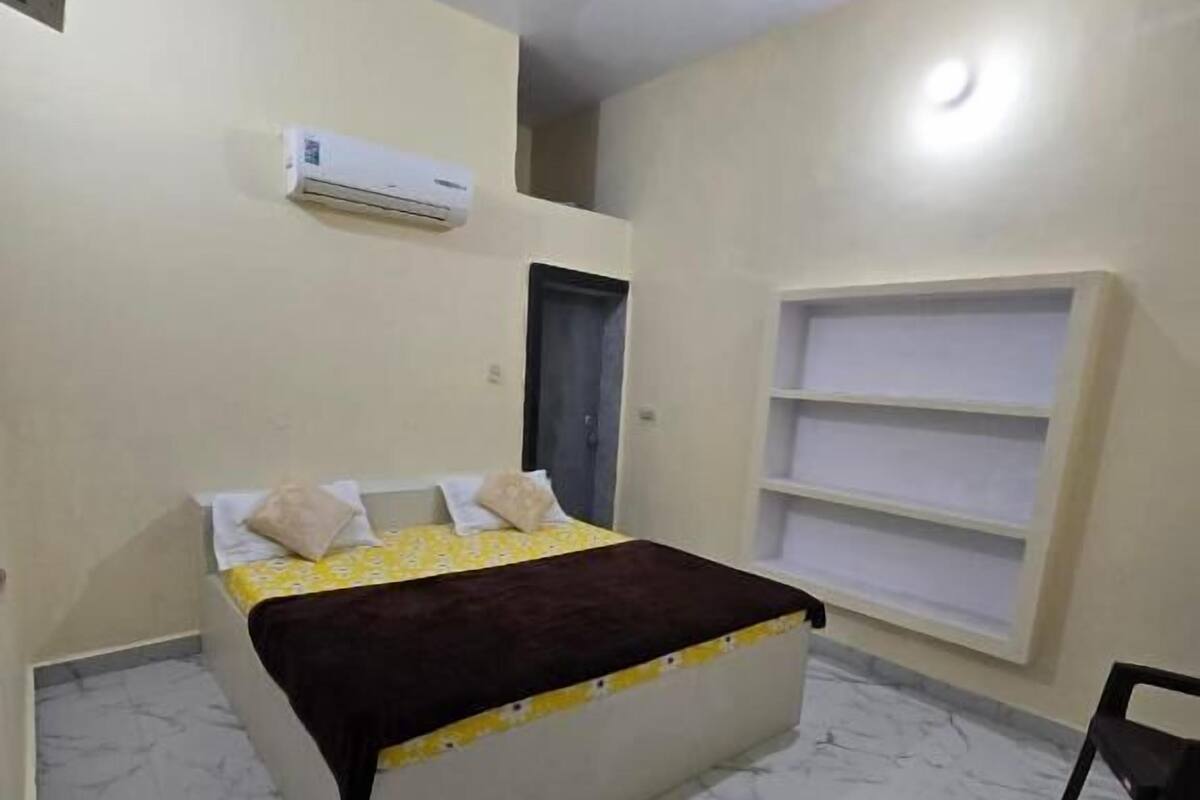 Ein Schlafzimmer mit einem Bett, einem Deckenventilator, einer Klimaanlage, einer Tür und einem Fenster mit Regalen.