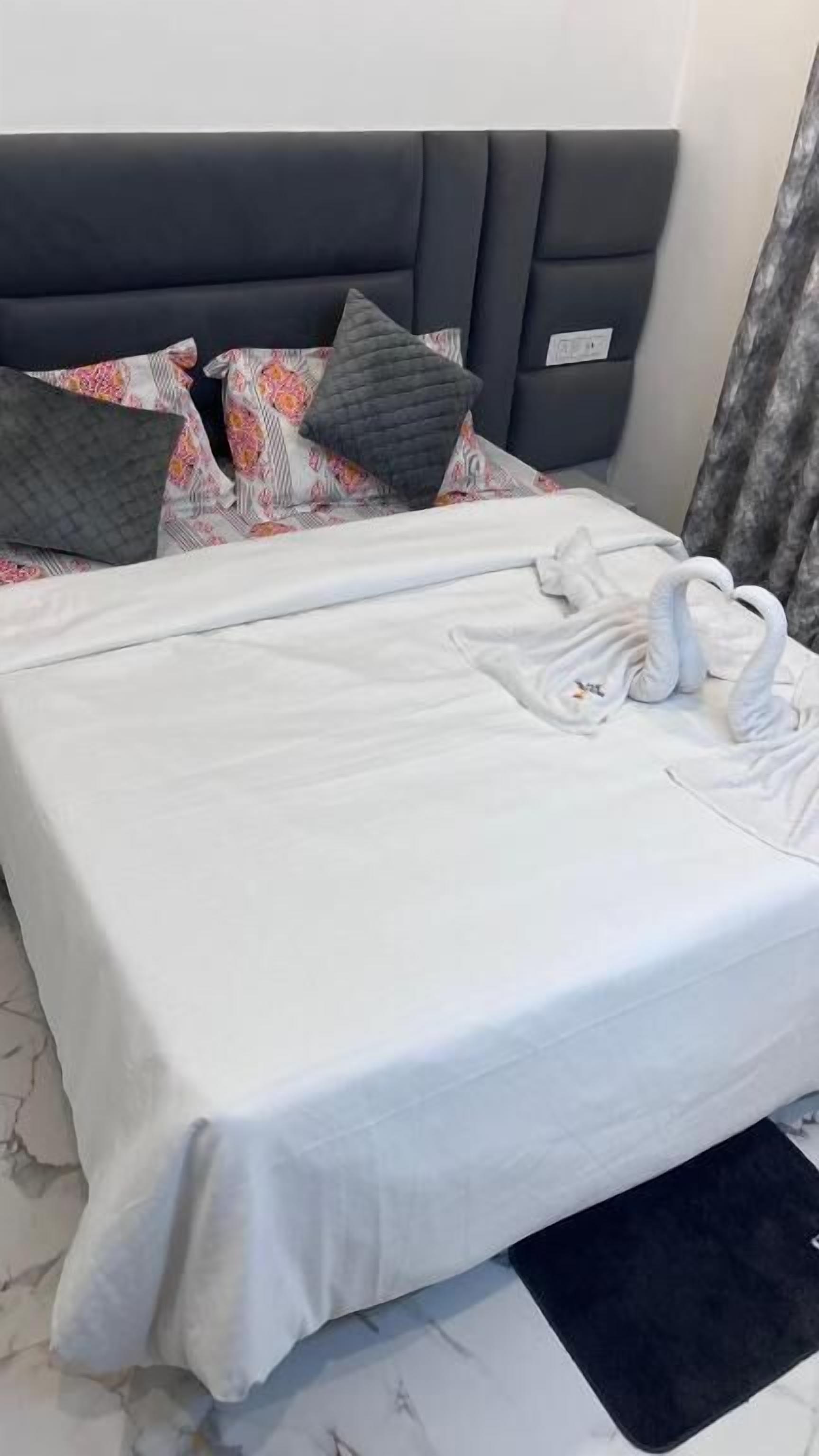 A neatly made bed with a white bedspread and pillows, a black headboard, and a black rug at the foot of the bed.