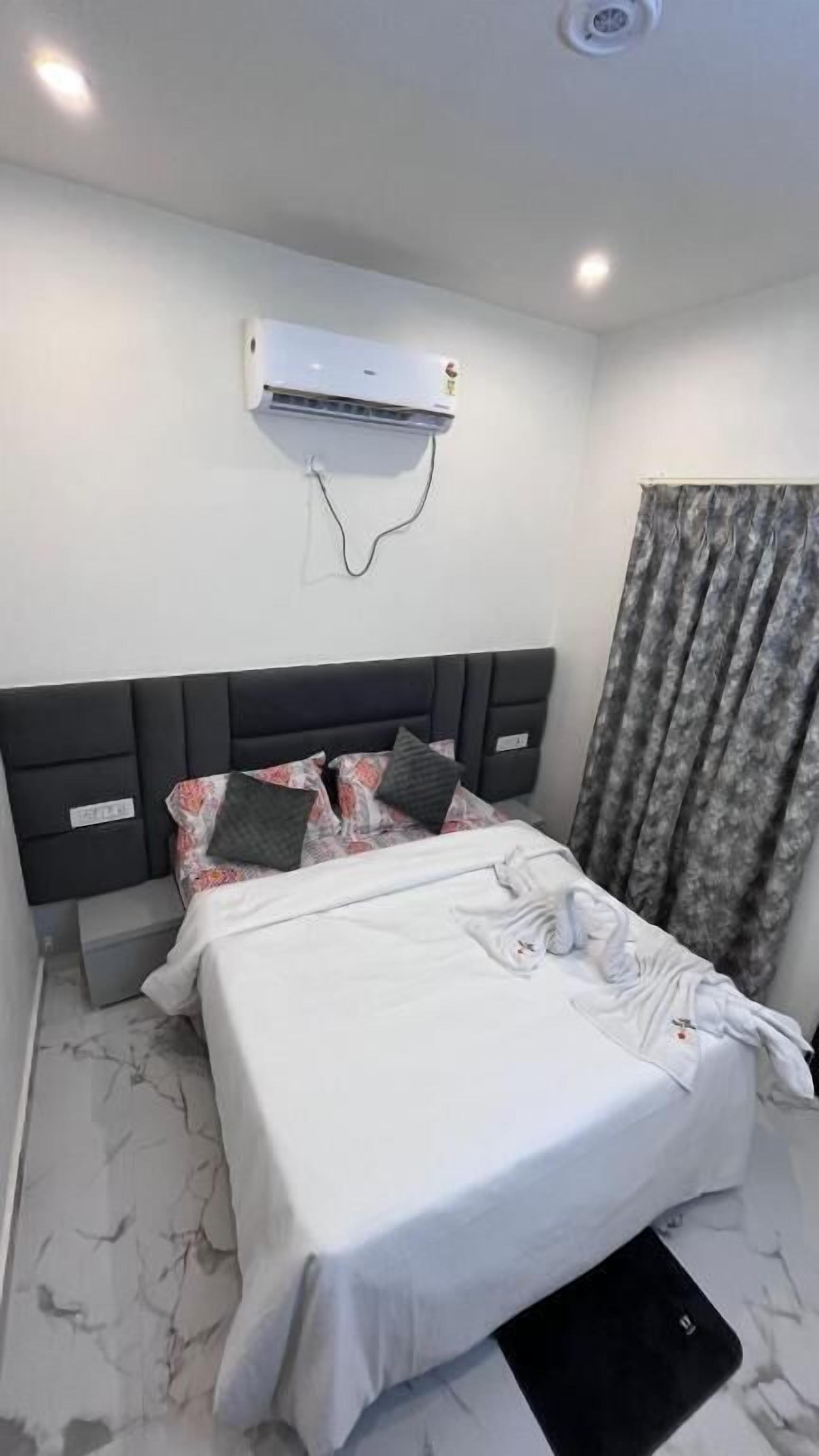 A hotel room with a bed, a headboard, a wall-mounted air conditioner, and a curtain.