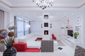Ein modernes Wohnzimmer mit einem weißen Sofa, roten Ziertelementen, einer Kristallleuchtre und einem Flachbildfernseher.