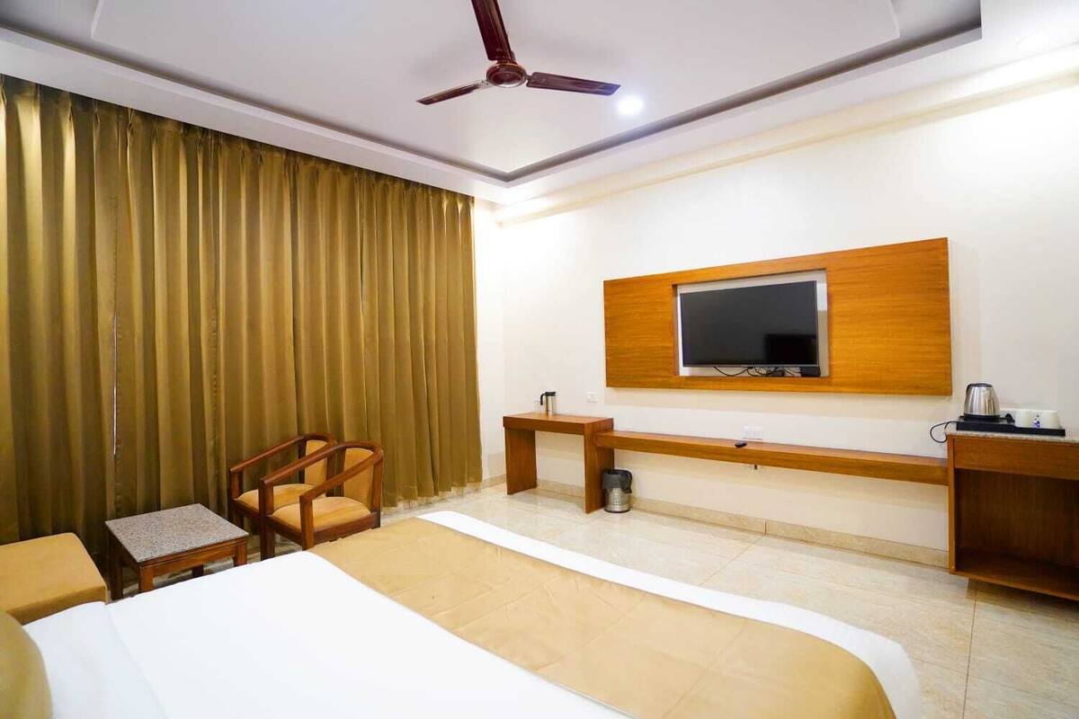 A hotel room with a bed, a desk, a chair, a TV mounted on the wall, and a ceiling fan.