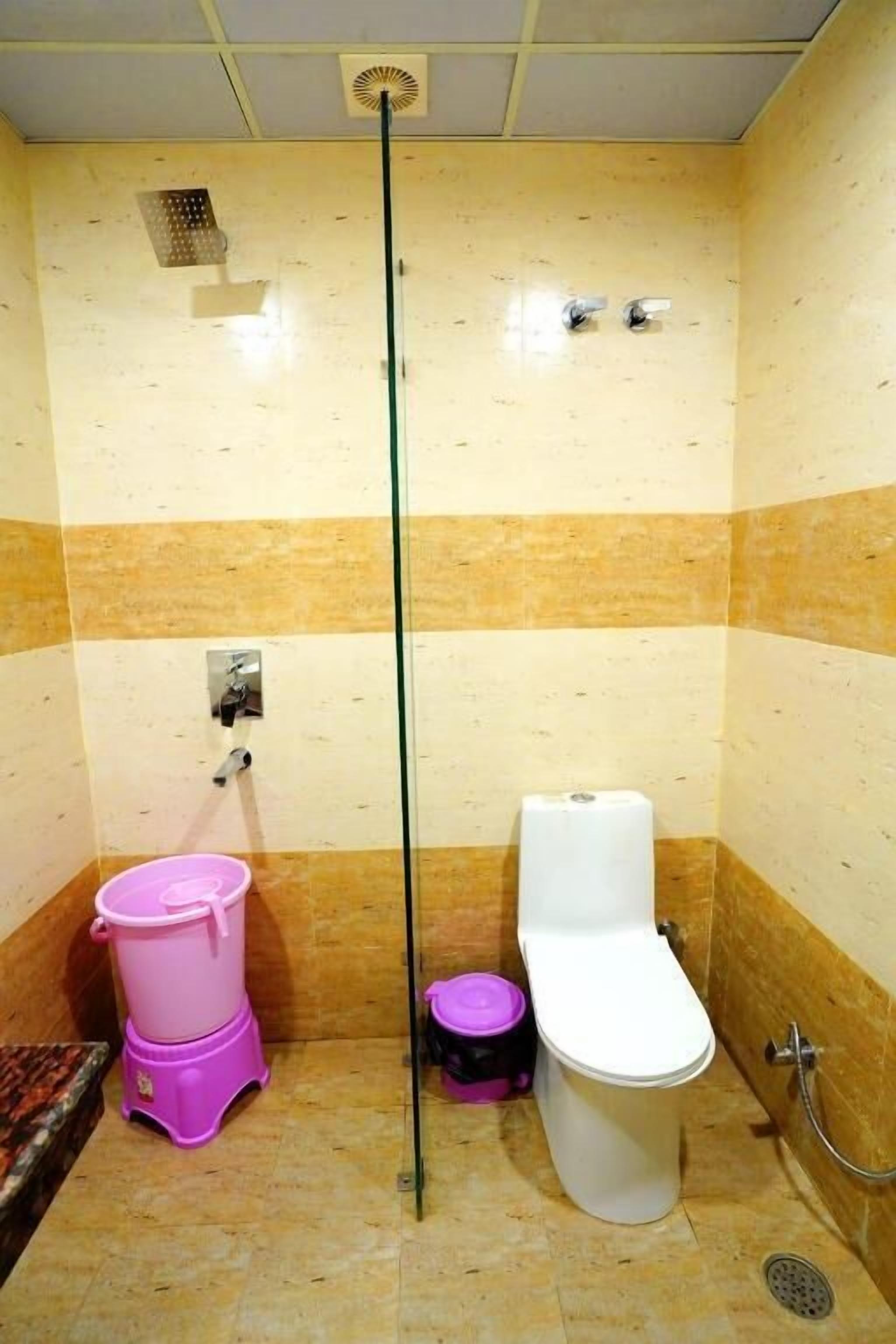 A small bathroom with a toilet, a shower, and a pink trash bin.