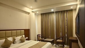 Ein Hotelzimmer mit einem großen Bett, einem kleinen Tisch, zwei Stühlen, einem Fernseher und einem Vorhang.