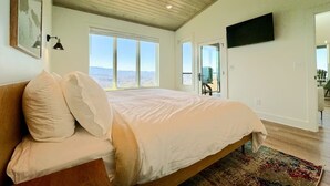 Een slaapkamer met een bed, een plafondventilator, een groot raam en uitzicht op het landschap.