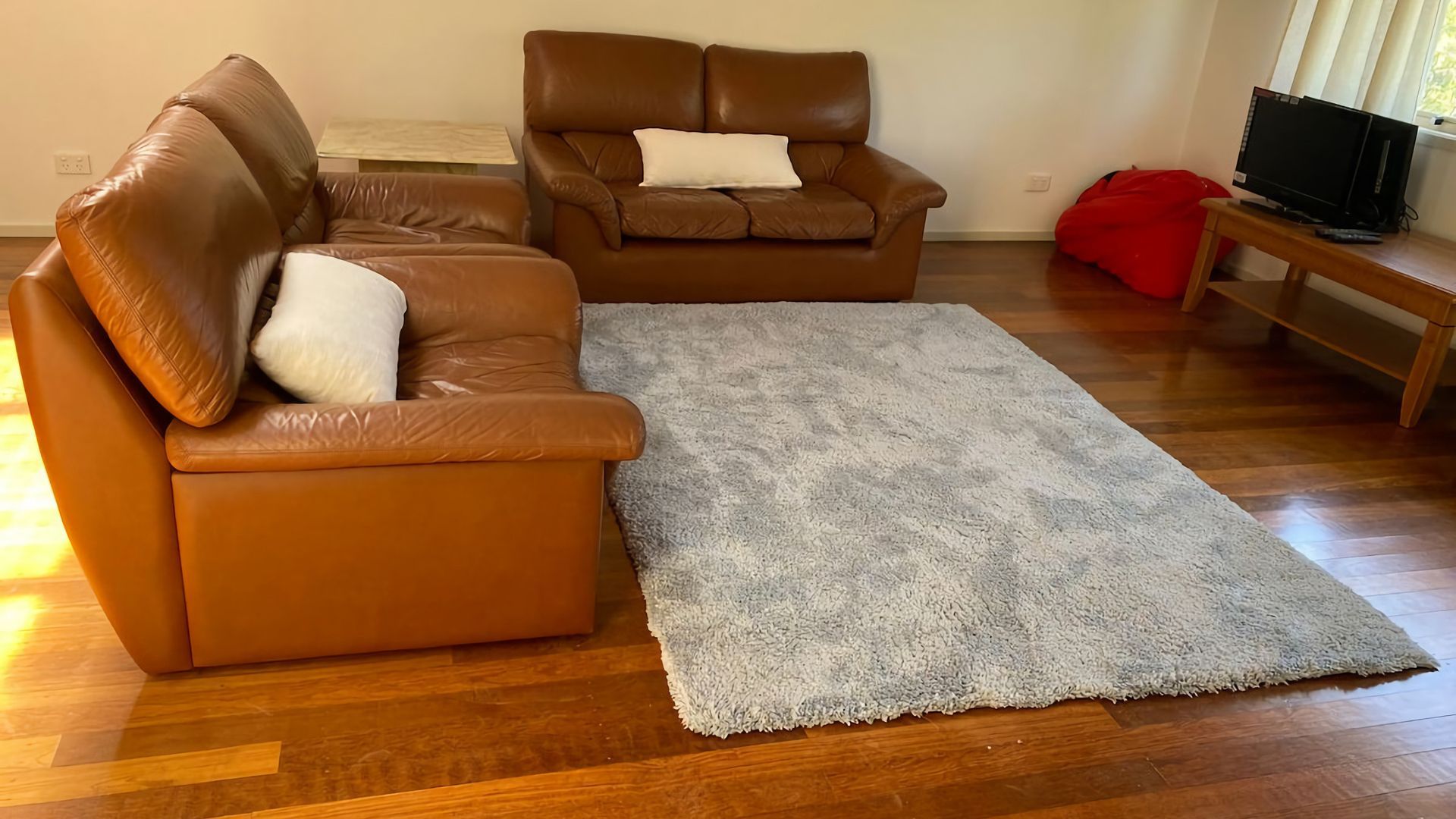 Un salon avec un canapé en cuir marron, un fauteuil assorti, un tapis gris et une table basse en bois.