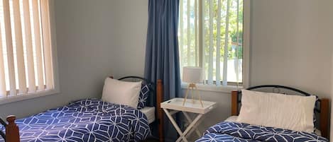 Une chambre avec deux lits simples, une petite table avec une lampe et une fenêtre avec des rideaux.