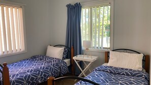 A room with two single beds, a small table with a lamp, and a window with curtains.