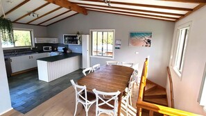 Een ruime keuken met een centraal eiland, witte kasten en een eethoek met een houten tafel en witte stoelen.