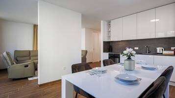A modern living room with a sofa, a dining table set for two, and a kitchen area with cabinets and appliances.