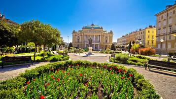 A square with a central monument, surrounded by benches and a flower garden.