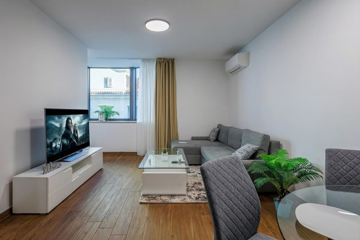 A modern living room with a flat-screen TV, a sofa, a coffee table, and a potted plant.