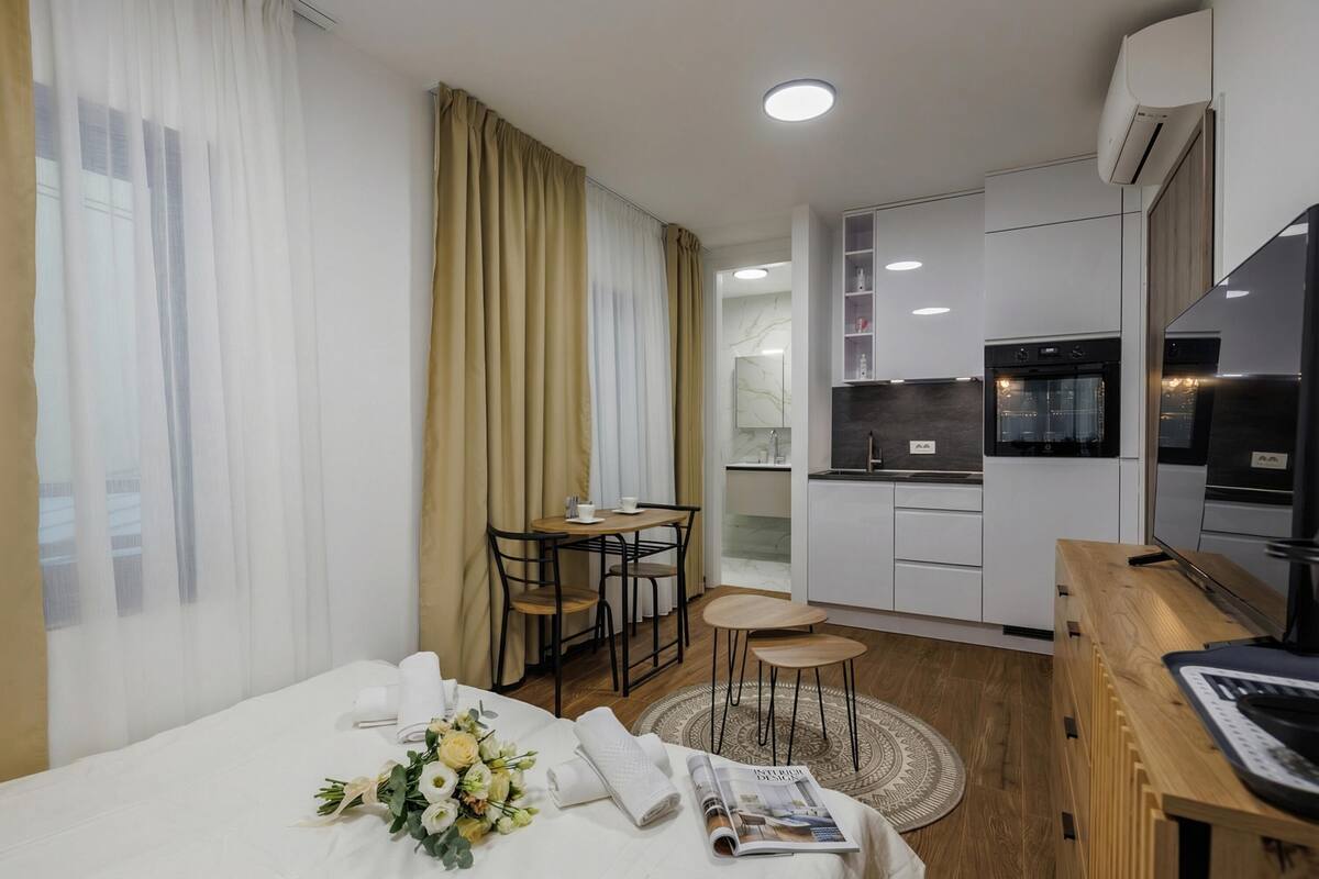 A hotel room with a bed, a small dining table, a kitchen area, and a TV.