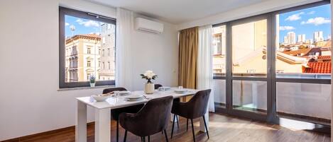 A dining area with a table set for two, large windows, and a view of the cityscape.