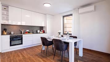 A modern kitchen with white cabinetry, a built-in oven, and a dining area with a white table and two chairs.