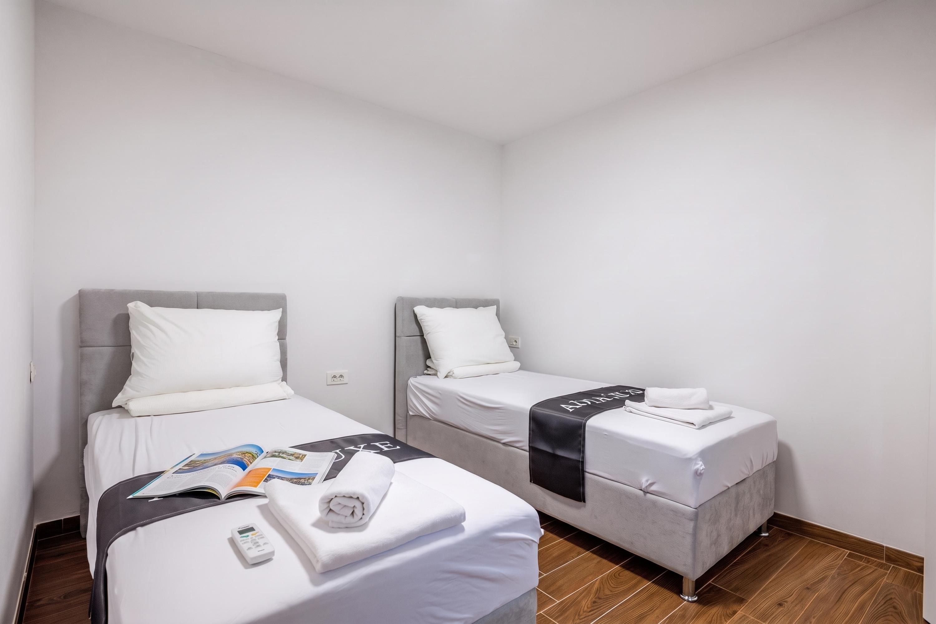 Habitación de hotel con dos camas individuales, cada una con cabecera gris, ropa de cama blanca y toalla negra.