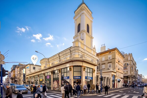 A street view with a prominent building featuring a tower and a corner entrance.