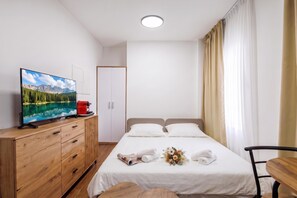 A hotel room with a bed, a TV on a wooden cabinet, a coffee machine, and a window with curtains. - City Apartments (Rijeka)