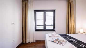 A hotel room with a bed, a window with curtains, a bedside table with a lamp, and a magazine on the bed.