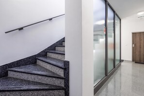 A staircase with granite steps and a metal handrail, leading to a room with a wooden door and a glass wall. - City Apartments (Rijeka)